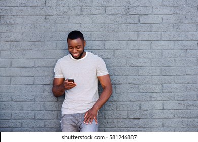 Portrait Of Smiling Man With Mobile Phone Leaning On Brick Wall