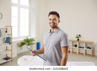 Portrait of smiling man physiotherapist with patient card in own cabinet in hospital. Happy male masseur or therapist ready for clients in wellness clinic. Healthcare and medicine concept.