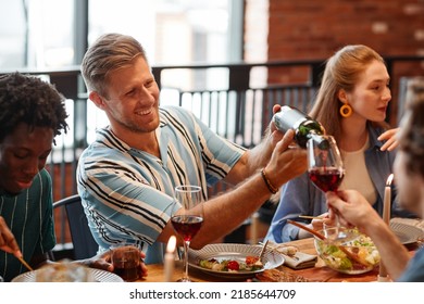 Portrait of smiling man pouring wine into glass while enjoying dinner party with friends in cozy setting - Powered by Shutterstock