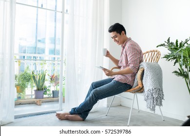 Portrait of a smiling man relaxing on chair new window using table and holding coffee cup. - Powered by Shutterstock