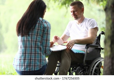 Portrait of smiling man sitting in wheelchair with papers. Handsome middle aged person in white shirt. Woman holding folder with documents. Working moments. Business and disabled people concept - Shutterstock ID 1767256505