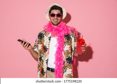 Portrait of smiling man wearing boa using cellphone while drinking soda isolated over pink background - Shutterstock ID 1775198120