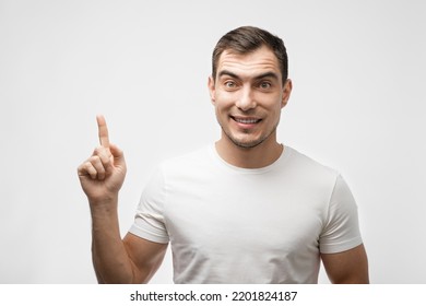 Portrait Of Smiling Man In White T-shirt With Finger Points Up On White Background For Advertising, Mockup, Copy Space