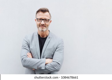 Portrait smiling mature bearded man wearing glasses standing and arms crossed against bright background