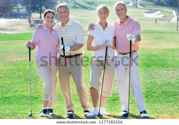Portrait of smiling mature couple with friends\
on golf course\
together