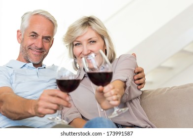 Portrait of a smiling mature couple with wine glasses sitting on sofa at home - Powered by Shutterstock