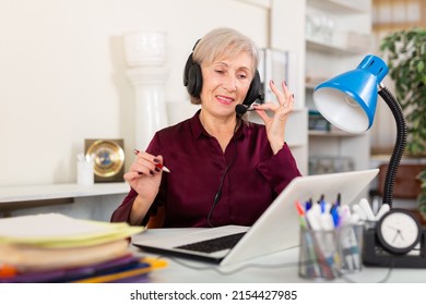 Portrait Of Smiling Mature Female Employee In Earphones Looking At Laptop Screen At Workplace In Office