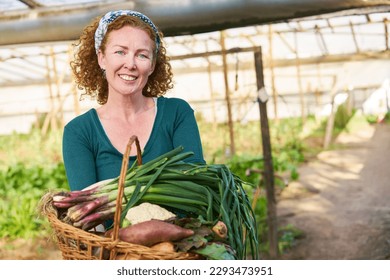 Portrait of smiling mature female farmer holding fresh vegetables basket in farm - Powered by Shutterstock