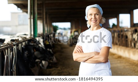 Portrait of smiling mature female farmer standing near cows at the cow farm