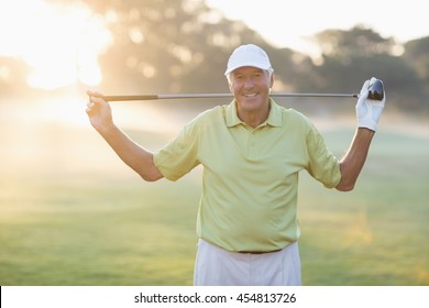 Portrait of smiling mature golfer carrying golf club while standing on field