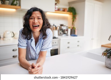 Portrait Of Smiling Mature Hispanic Woman Wearing Pyjamas Spending Morning At Home In Kitchen