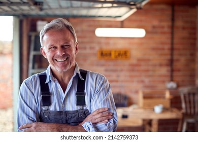 Portrait Of Smiling Mature Male Wearing Overalls In Garage Workshop