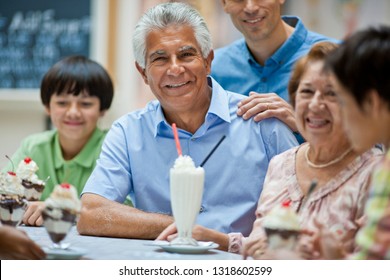 Portrait of a smiling mature man surrounded by family at an ice cream parlor.
