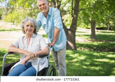 Portrait Of A Smiling Mature Man With Woman Sitting In Wheel Chair At The Park