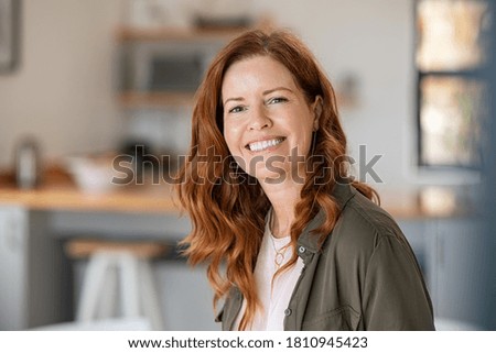 Photo of Portrait of smiling mature woman looking at camera with big grin. Successful middle aged woman at home smiling. Beautiful mid adult lady with long red hair enjoying whitening teeth treatment.