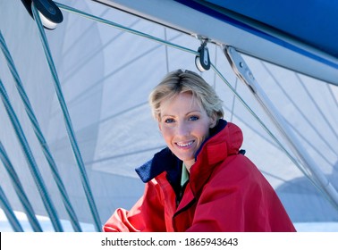 Portrait Of A Smiling Mature Woman In Red Jacket Sitting On The Deck Of The Sailing Boat Below Sail.