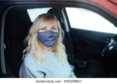 Portrait Of Smiling Mature Woman Wearing Fabric Masks Sitting In Her Red Car. Female Adult Getting Tested At A Drive-Thru Testing Site. European Covid-19 Coronavirus Vaccine Clinic Looking At Camera.