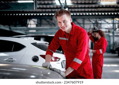 Portrait of smiling mechanic man in red uniform standing around vehicle cars at garage, auto technician checking and repairing maintenance customer car automobile at repair service shop.