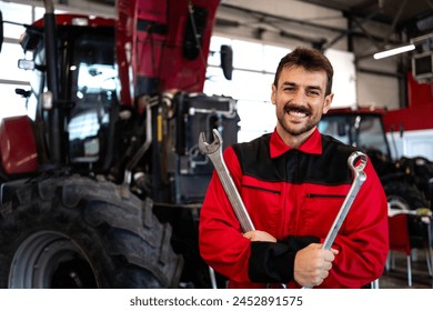 Portrait of smiling mechanic standing by the tractor inside workshop maintaining agricultural machines. - Powered by Shutterstock