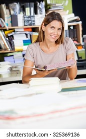 Portrait Of Smiling Mid Adult Female Worker Holding Spiral Book In Factory