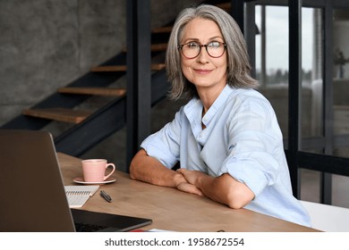 Portrait Of Smiling Middle Age 60s Aged Business Woman Working At Home Office With Laptop, Headshot Of Happy Woman Worker Or Ceo Posing For Corporate Photoshoot, Looking At Camera.