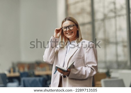 Portrait of smiling middle age businesswoman with note book standing on office background
