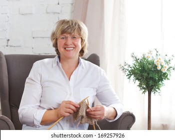 Portrait of a smiling middle age woman knitting on spokes at home - Shutterstock ID 169257926