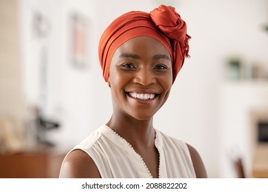 Portrait of smiling middle aged African american woman with headscarf at home. Mid adult black woman with turban looking at camera. Happy mid mature lady wearing traditional african scarf on head.