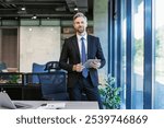 Portrait of smiling middle aged businessman standing with digital tablet at corporate office