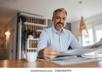 Portrait of a smiling middle aged businessman reading newspaper, sitting at table and drinking coffee, at home. - Powered by Shutterstock