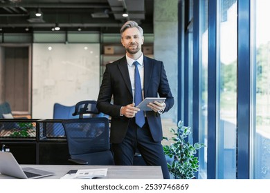 Portrait of smiling middle aged businessman standing with digital tablet at corporate office - Powered by Shutterstock