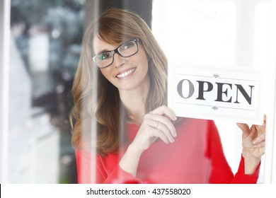 Portrait Of A Smiling Middle Aged Woman Holding Up A Sign On Opening Day Of Her Small Business.