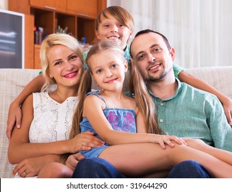 Portrait Of Smiling Middle Class Caucasian Family At Home Interior. Focus On Girl