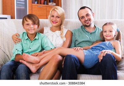 Portrait Of Smiling Middle Class Family With Two Children At Home Interior. Focus On Woman