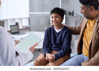 Portrait of smiling Middle Eastern boy visiting doctor in clinic with father supporting - Powered by Shutterstock