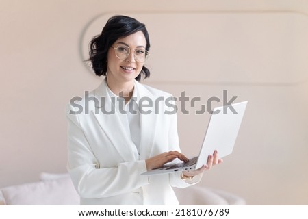 Portrait of smiling middle-aged brunette woman in white jacket. With silver laptop in hand. Looks into camera. With copy space.