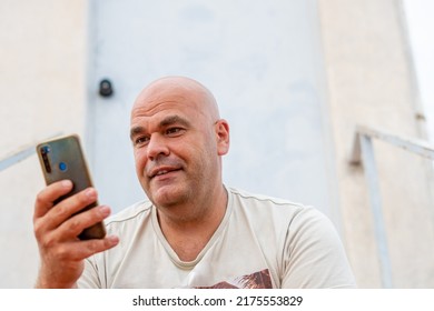 Portrait Of A Smiling Middle-aged Spanish Man, Using A Mobile Phone, Outdoors.