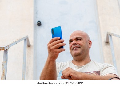 Portrait Of A Smiling Middle-aged Spanish Man, Using A Mobile Phone, Outdoors.