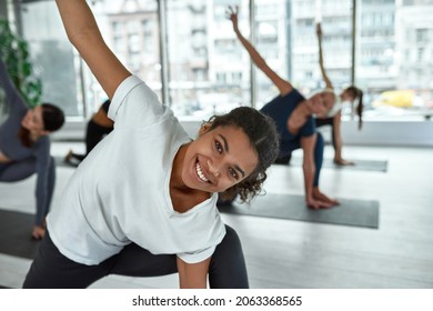 Portrait of smiling millennial African American girl in sportswear do sports stretching yoga at group class. Happy ethnic young woman have pilates workout training in gym. Healthy lifestyle concept. - Powered by Shutterstock