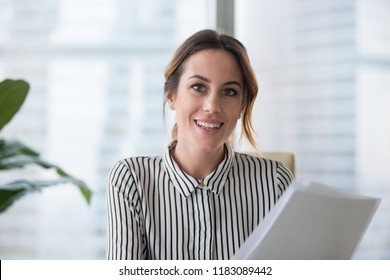 Portrait of smiling millennial businesswoman holding documents looking at camera, headshot of happy woman worker or female ceo posing with paperwork making picture at corporate close up photoshoot.