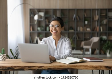 Portrait Of Smiling Millennial Indian Female Student Sit At Desk At Home Study Online On Laptop. Happy Young Mixed Race Woman Use Computer Take Distant Course Or Training. Education Concept.