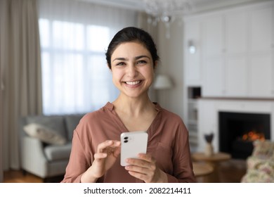 Portrait of smiling millennial indian woman looking at camera, holding cellphone in hands, feeling excited of getting message with good news, enjoying spending time online, modern tech addiction.
