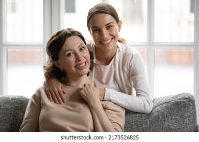 Portrait of smiling millennial woman cuddling happy beautiful middle aged mother sitting on sofa. Happy multigenerational female loving family looking at camera, posing for photo together at home. - Powered by Shutterstock