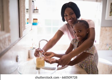 Portrait of smiling mother assisting daughter while washing hands in bathroom at home, Coronavirus hand washing for clean hands hygiene Covid19 spread prevention