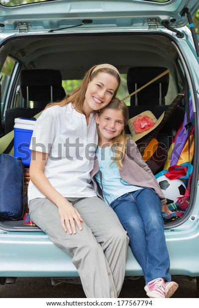 Portrait of a smiling mother and daughter sitting\
in car trunk while on\
picnic