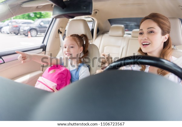 portrait of smiling mother driving car with daughter\
pointing away near by