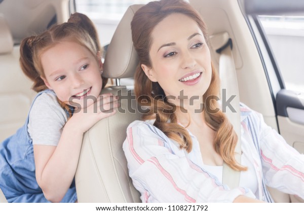 portrait of smiling mother driving car with daughter\
on passengers seat