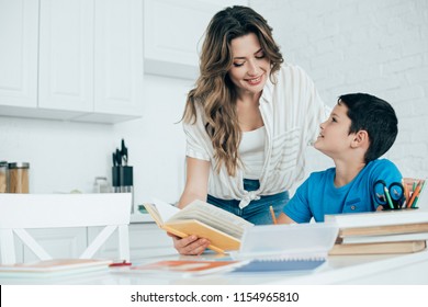 portrait of smiling mother helping son with homework in kitchen at home