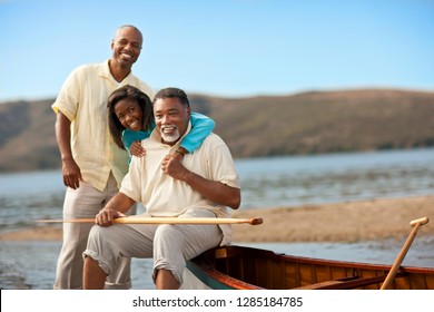 Portrait Of A Smiling Multi Generational Family Sitting Near A Canoe On A Beach.