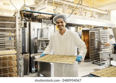 Portrait of smiling multicultural food factory chef holding tray with raw biscuits and preparing it for baking. - Powered by Shutterstock